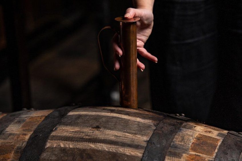 A person holding a copper tap over a wooden barrel. 2