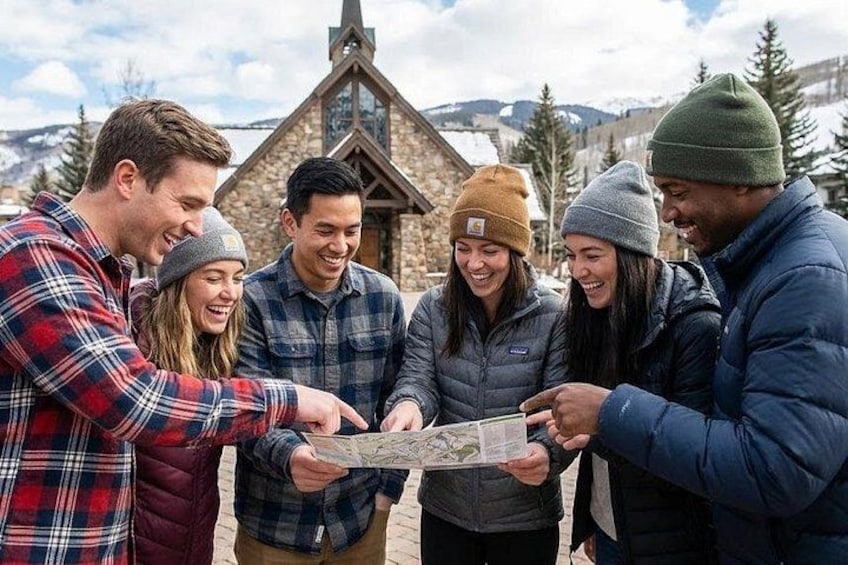 Eine Gruppe von Personen betrachtet draußen eine Karte, im Hintergrund ist ein Steinhaus zu sehen. 1