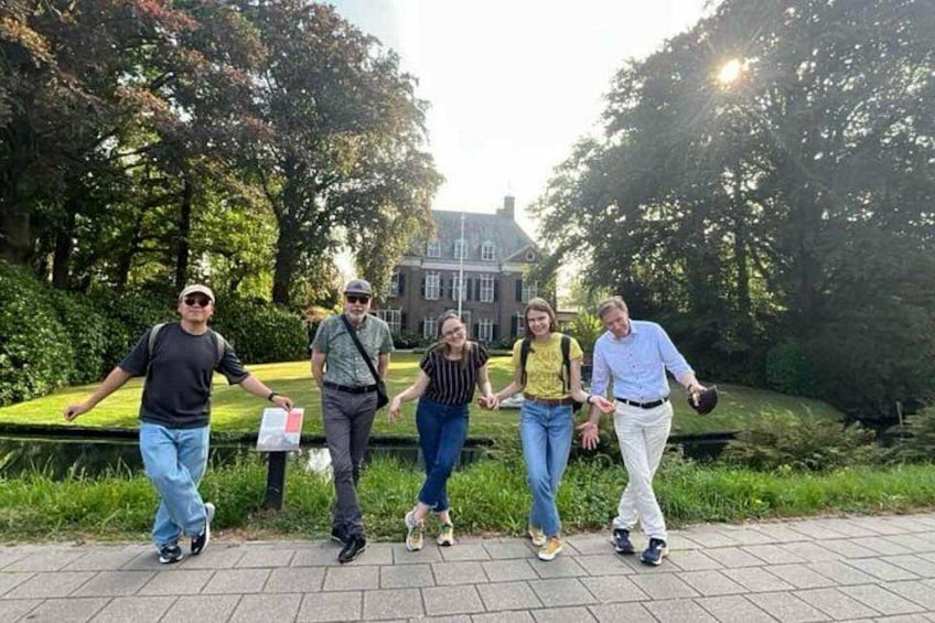 Eine Gruppe von Menschen geht auf einem gepflasterten Weg in einem Park, im Hintergrund sind Bäume und ein Gebäude zu sehen. 4