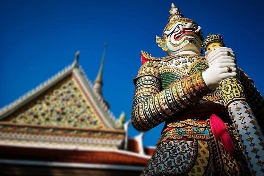 A colorful statue with intricate patterns, holding a staff, and a traditional building with a pointed roof in the background. 2