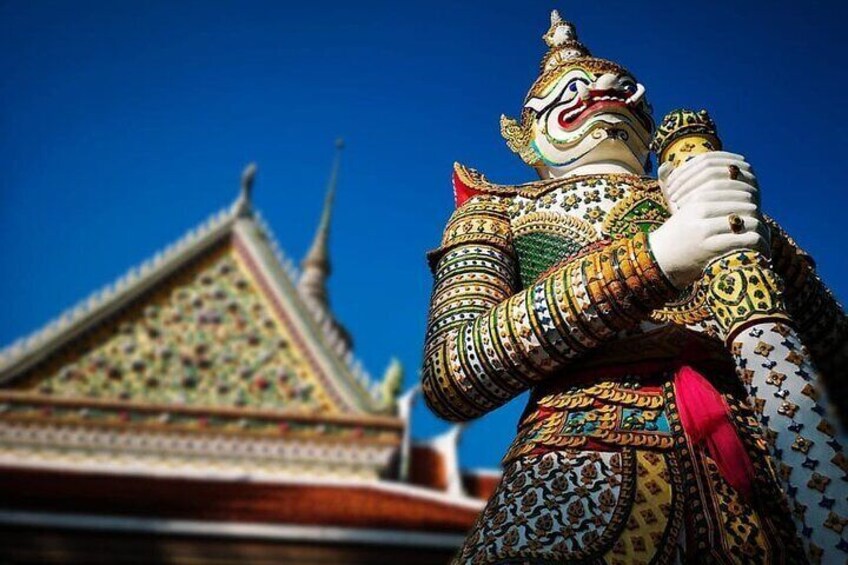 A colorful statue with intricate patterns and a pointed hat, standing in front of a temple with a pointed roof. 3