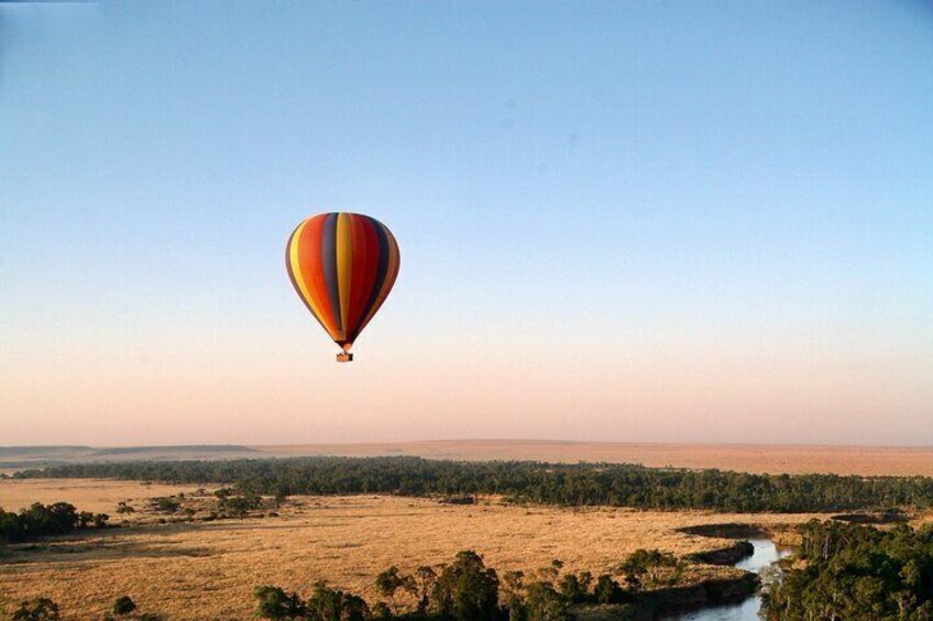 Un globo aerostático volando sobre un paisaje con un río y vegetación escasa. 2