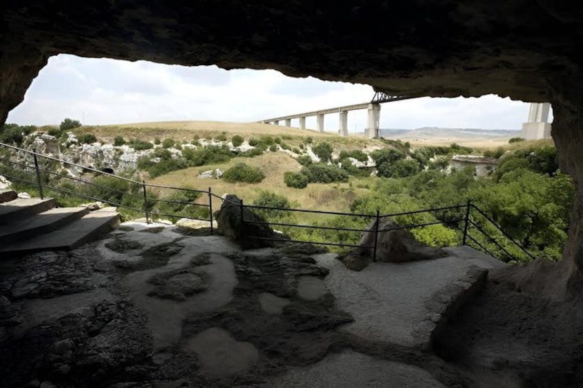 A cave entrance with a view of a bridge and hilly landscape. 1