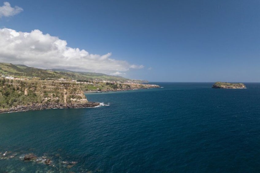 A coastal landscape with cliffs, a small island, and a clear blue sea. 2