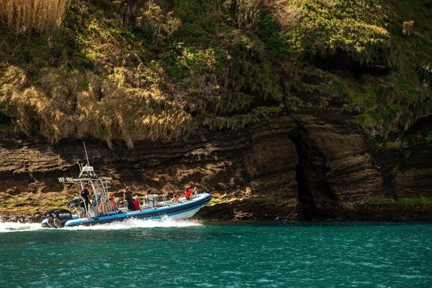 Una barca blu con passeggeri, vicino a una scogliera rocciosa e acqua cristallina. 2
