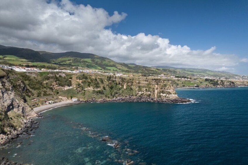 A coastal landscape with a beach, rocky cliffs, and a clear blue sea. 5