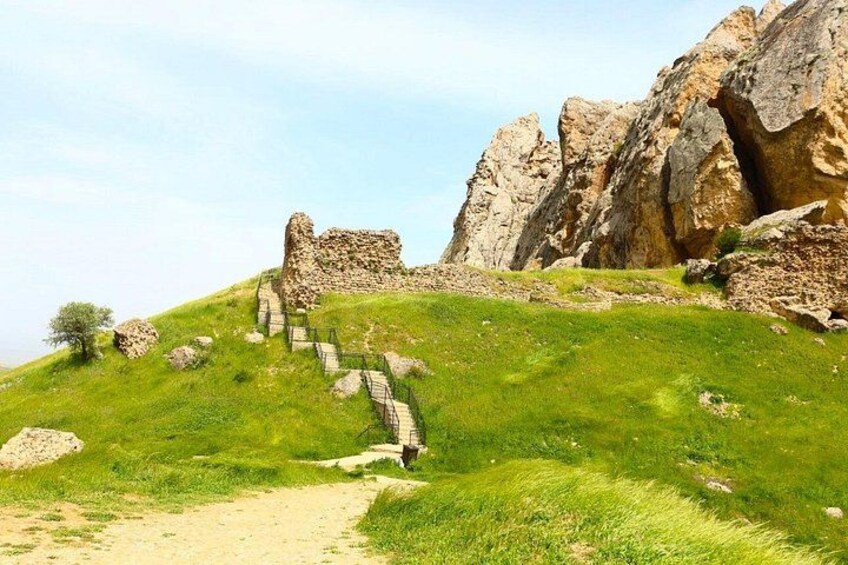 A grassy hill with a stone staircase leading up to a rocky outcrop. 1