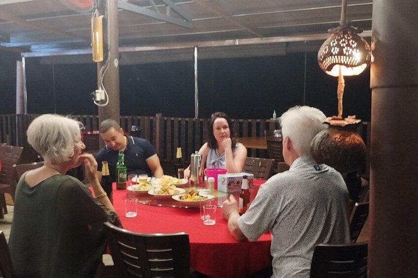 Eine Gruppe von Personen speist an einem Tisch mit roten Tischdecken, umgeben von Stühlen und einer Hängelampe. 2