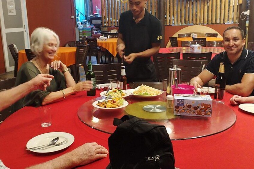 Een groep mensen dineert aan een ronde tafel met eten en drinken. 2