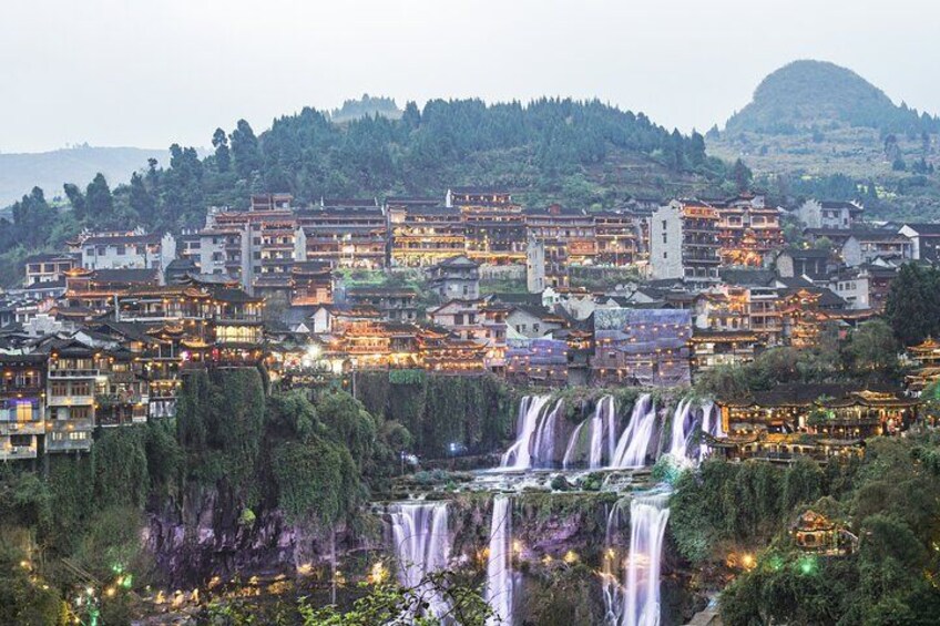 A town with multiple waterfalls, traditional buildings, and a hilly backdrop. 2