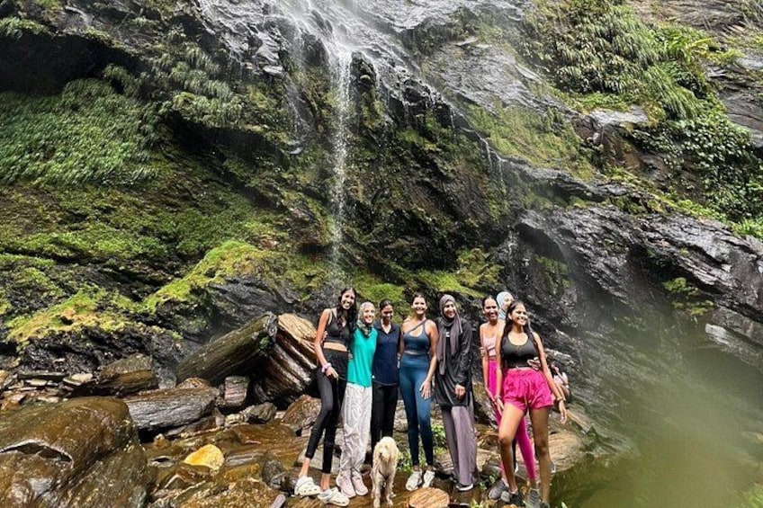 Een groep mensen staat op rotsen nabij een waterval in een bebost gebied. 3