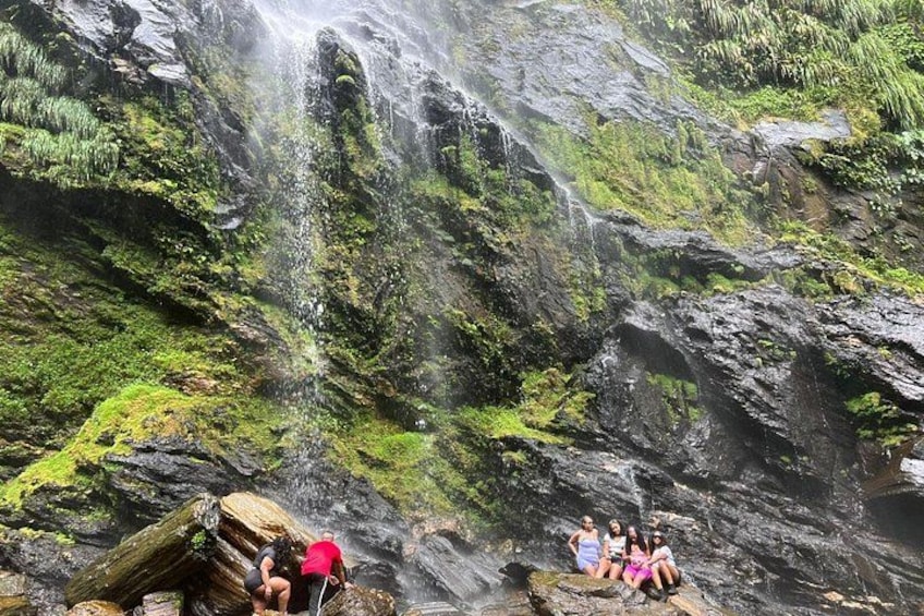 Een waterval die over een rotsachtige klif stroomt, met begroeide rotsen en beplanting. 4