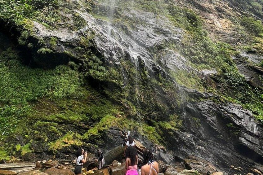 Een waterval die over een rotsachtige klif stort, met mosbedekte oppervlakken en enkele mensen die het bekijken. 2
