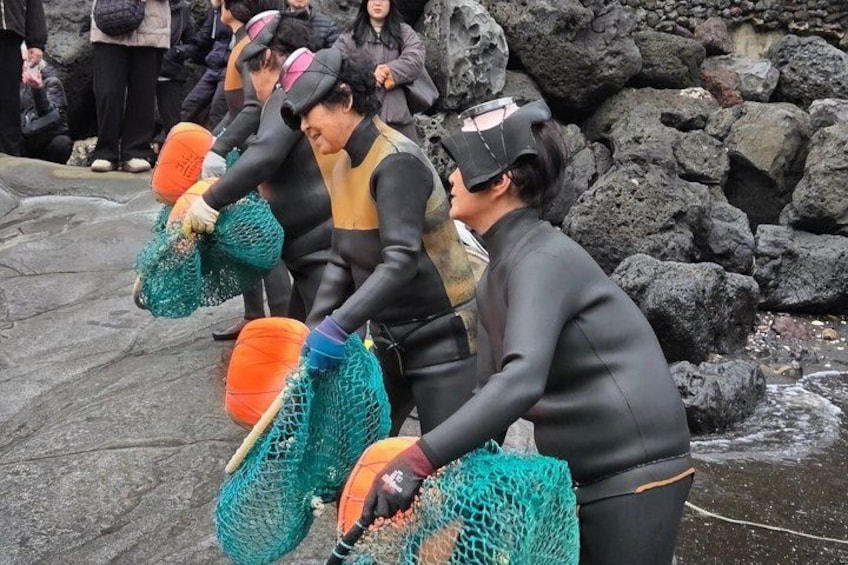 People in wetsuits holding nets near a rocky shoreline. 5