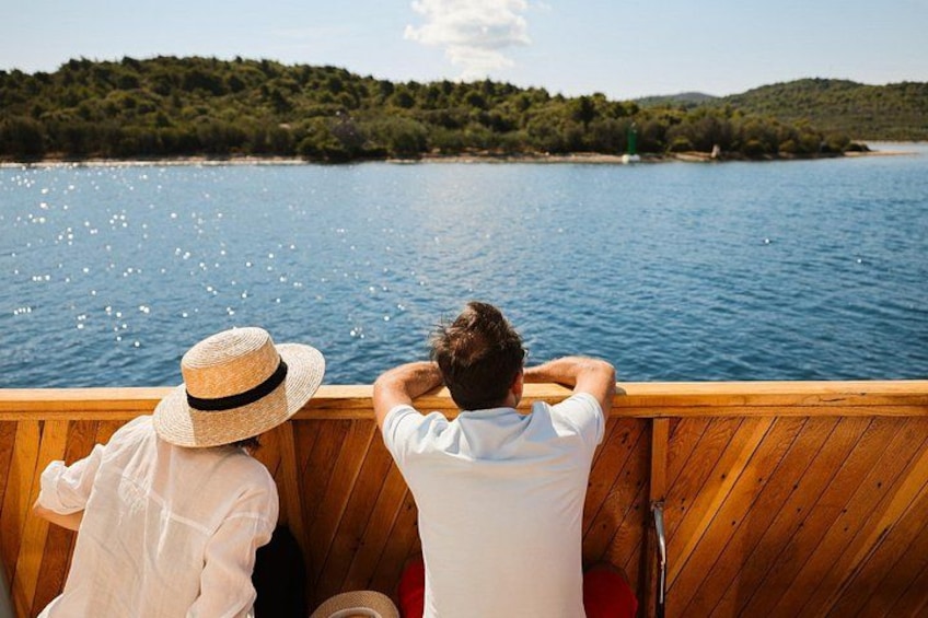 Two people on a wooden boat, looking at a calm lake with a forested shoreline. 1