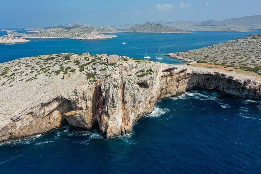 A coastal landscape with a prominent rock formation, a clear blue sea, and distant islands. 5