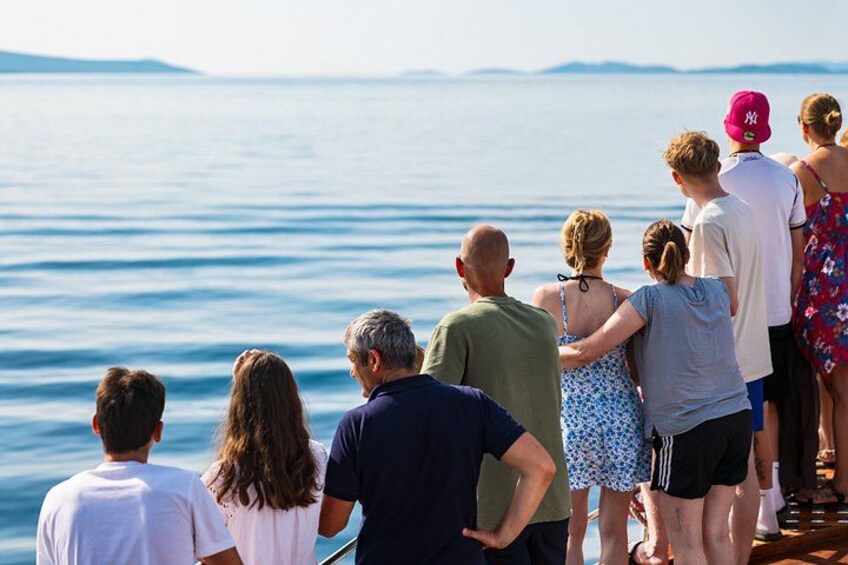 A group of people standing by a body of water with a clear view of the horizon. 2