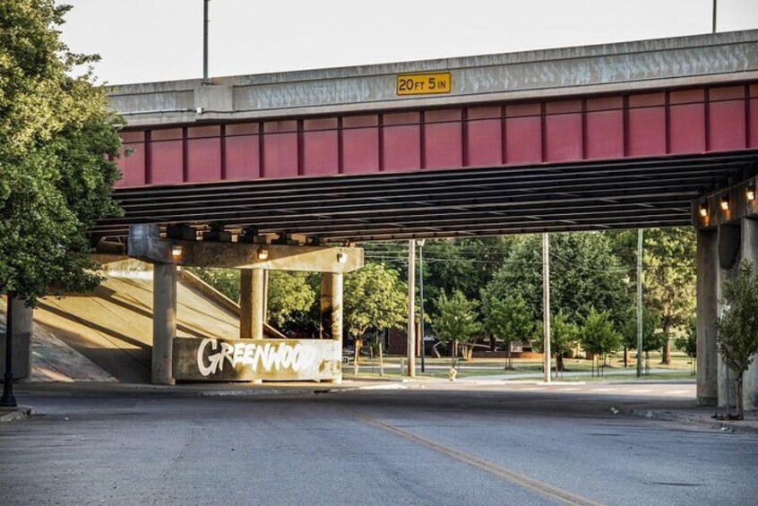 An overpass with a height limit sign, a street with a 'Greenwood' sign, and trees in the background. 3