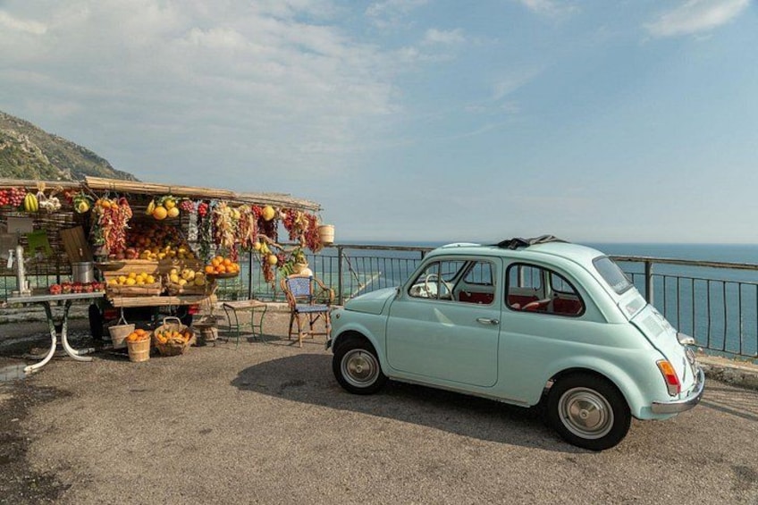Een klassieke auto geparkeerd langs de weg, nabij een fruitkraam. 2