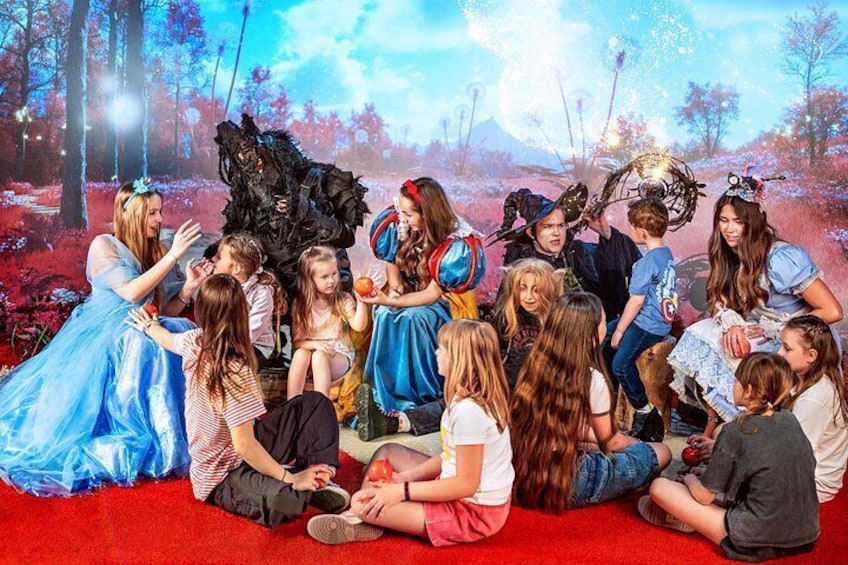 A group of people sitting on a red carpet in a forest setting with a fantasy-themed backdrop. 5