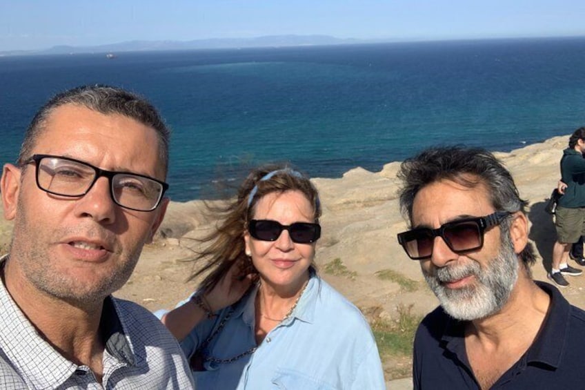 Three people standing on a rocky outcrop with a view of the ocean. 1