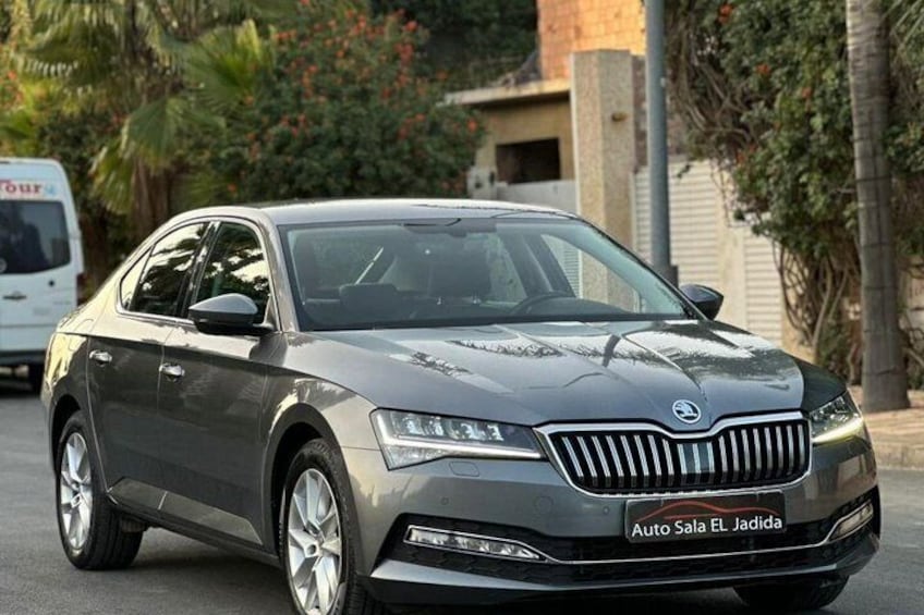A silver sedan parked on a street with a building and trees in the background. 3