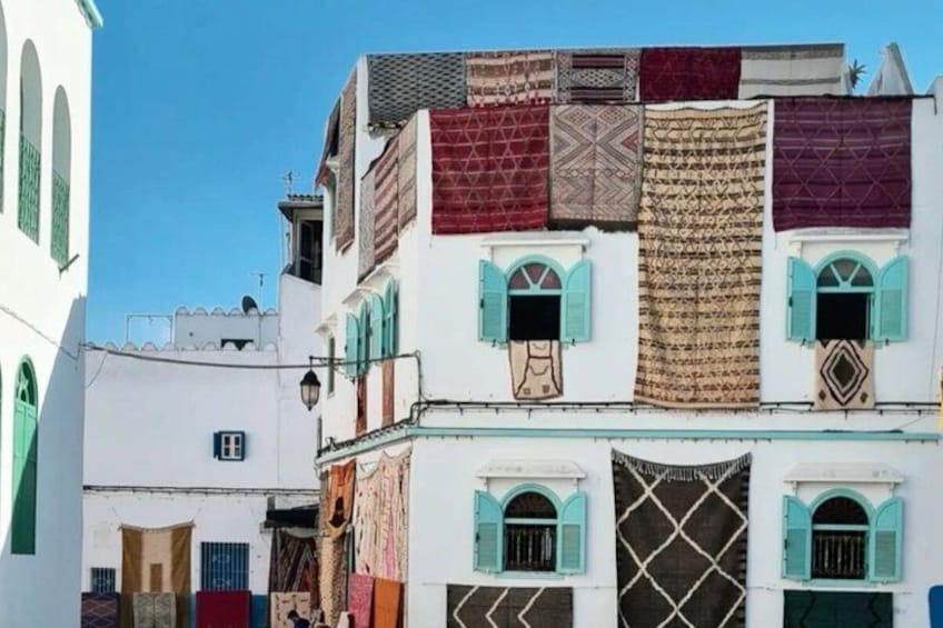 A narrow street with colorful buildings, some with shutters and others with patterned fabrics. 3