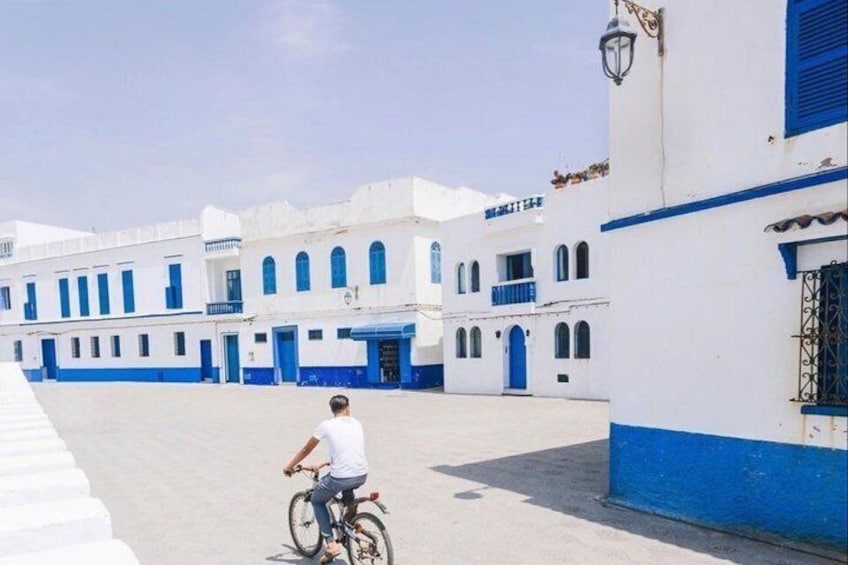 A person riding a bicycle in a courtyard with white and blue buildings. 1