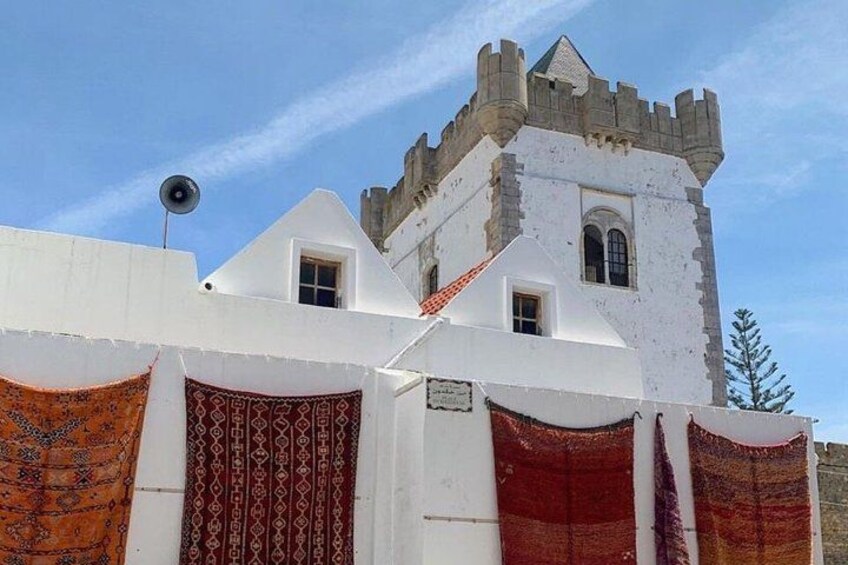 A white building with a tower, patterned fabric hanging in front, and a clear blue sky. 2