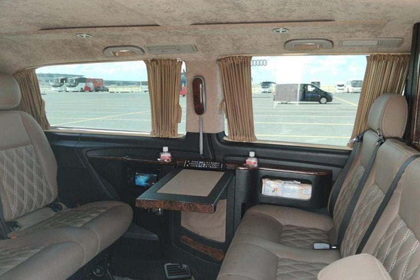 The interior of a bus with two seats, a small table, and a window with curtains. 2