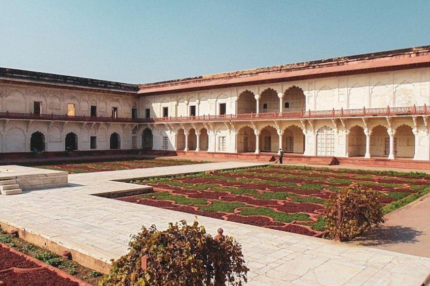 A courtyard with a patterned garden, white buildings with arches, and a clear sky. 3