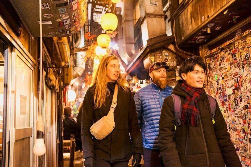 A narrow alley with people walking, illuminated by hanging lanterns and covered with stickers. 1