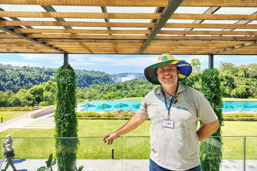Una persona parada en un espacio cubierto con vista a una piscina y follaje al fondo. 1