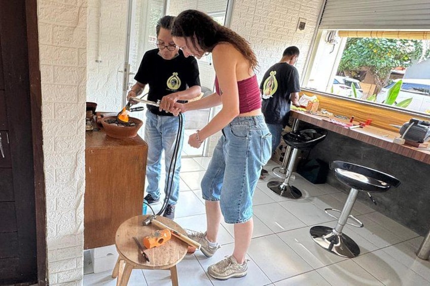 Eine Person verwendet einen Brenner an einem Kochtopf, eine weitere Person steht in der Nähe, und eine Küchenarbeitsplatte mit verschiedenen Gegenständen ist zu sehen. 5