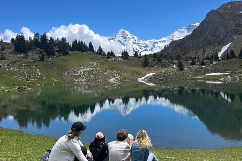 Un grupo de personas sentadas junto a un lago, con montañas al fondo. 1