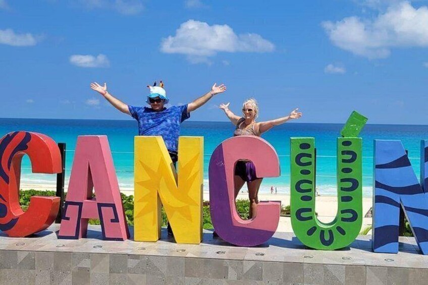 A beach with large colorful letters spelling 'CANCUN' and two people standing in front of them. 5