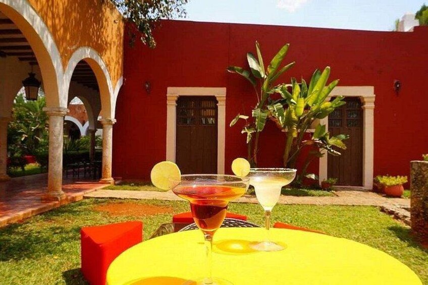 A yellow table with two drinks, a red building, and a courtyard with arches. 4