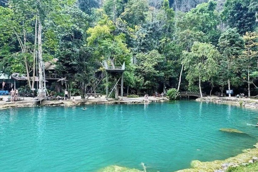 A turquoise lake surrounded by dense forest, with a small wooden structure and a bridge in the background. 3