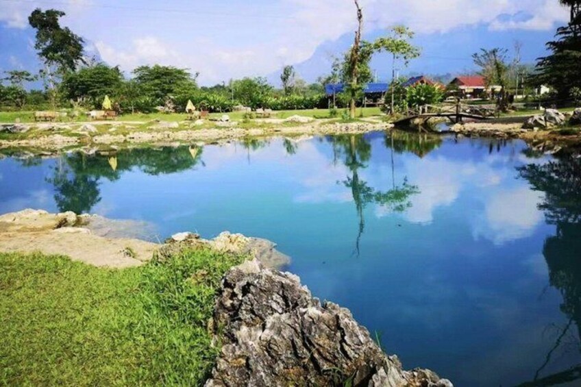 A calm pond with clear reflections, surrounded by greenery and a wooden bridge. 2