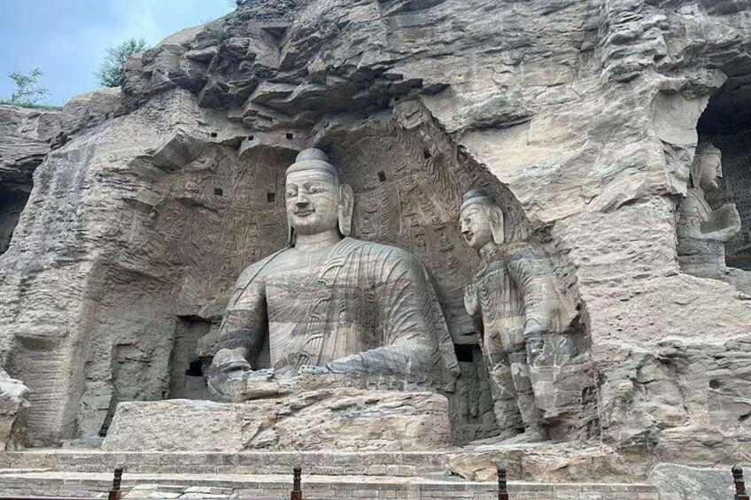 Una estatua de Buda tallada en roca de grandes dimensiones, con tallas intrincadas, rodeada de estatuas más pequeñas y un escarpado acantilado. 1