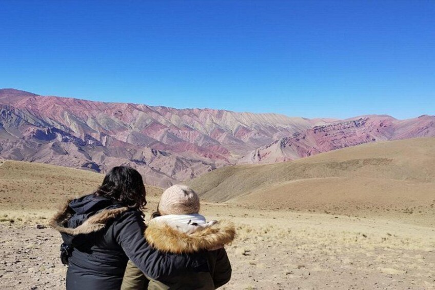 Two people standing on a barren landscape with mountains in the background. 2