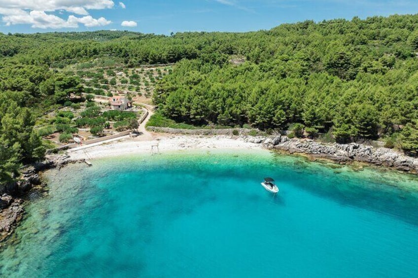A turquoise sea, a boat, and a forested hill. 1