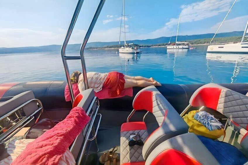 A boat with red and grey seats, a person lying on the edge, and calm water with boats in the background. 5