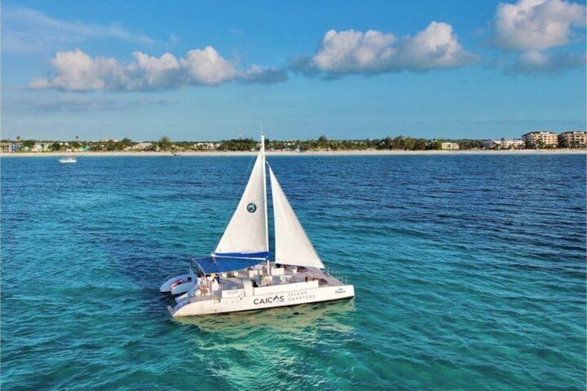 A sailboat named 'CAICAS' on turquoise waters with a clear sky and a distant shoreline. 2
