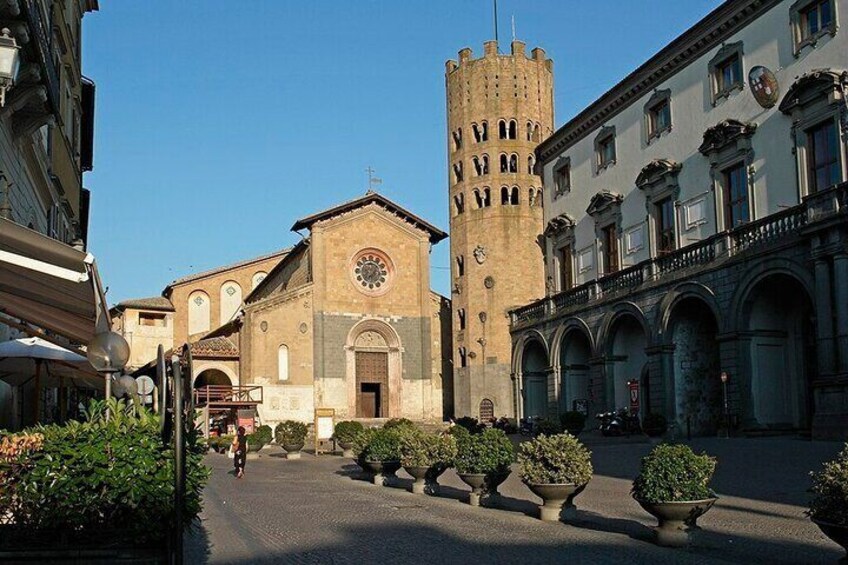Una plaza histórica con una iglesia, una torre alta y macetas con plantas. 3