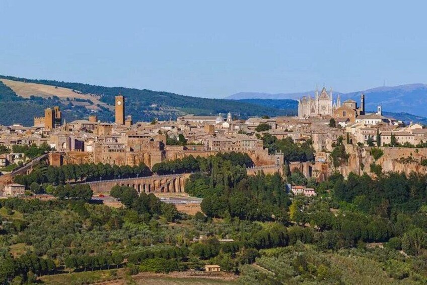 A historic cityscape with prominent architecture, including a cathedral and towers, surrounded by greenery and hills. 2