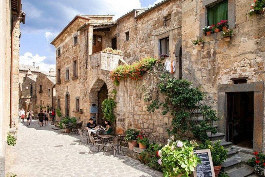 A stone building with a café, outdoor seating, and potted plants. 4