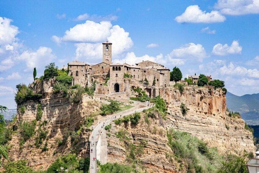 A historic stone building on a cliff with a winding road leading up. 1