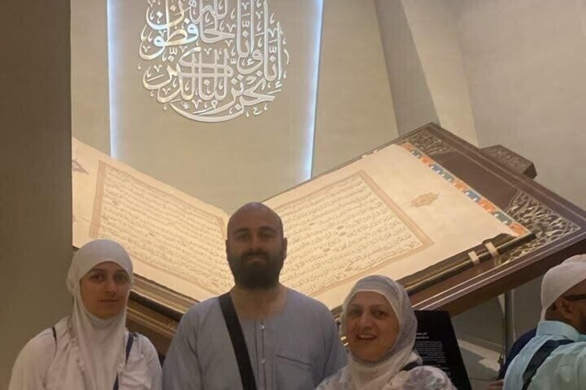 Eine Gruppe von Menschen steht vor einer großen, beleuchteten arabischen Kalligraphie und einem Manuskript. 3
