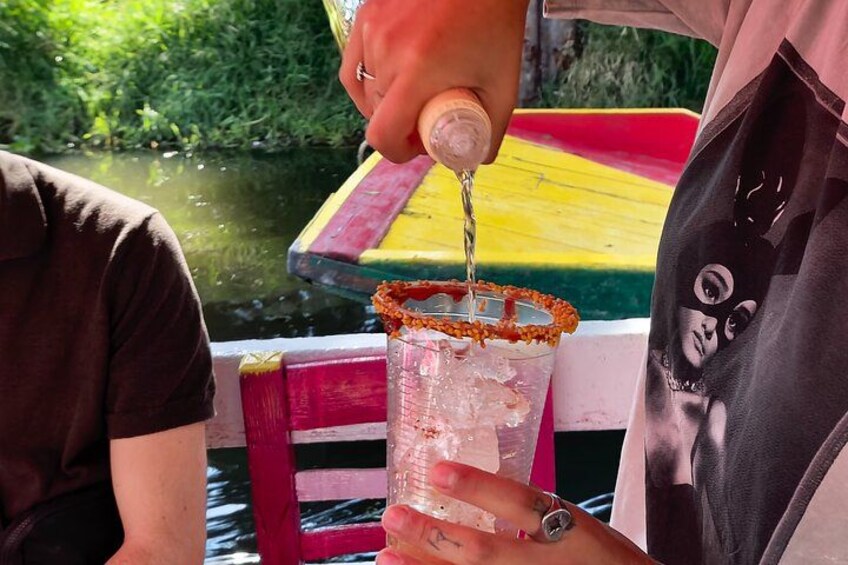 Iemand giet een drankje in een glas met zoutrand, zittend in een boot met een kleurrijke tafel en begroening op de achtergrond. 2